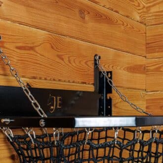 Black metal EZ-fill haynet on wooden wall, featuring chain attachments, slow-feed design for equine stalls.