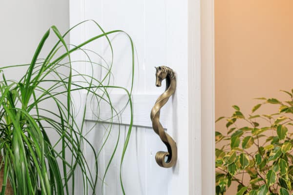 Decorative horse-head handle in an antique brass finish on a white sliding barn door.